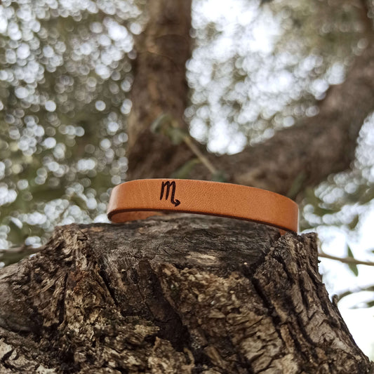 A brown leather bracelet with scorpio´s symbol engraved on it.