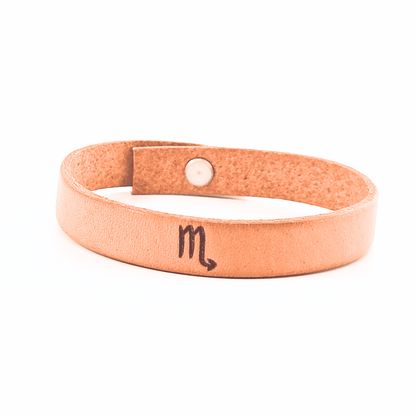 A brown leather bracelet with scorpio´s symbol engraved on it.