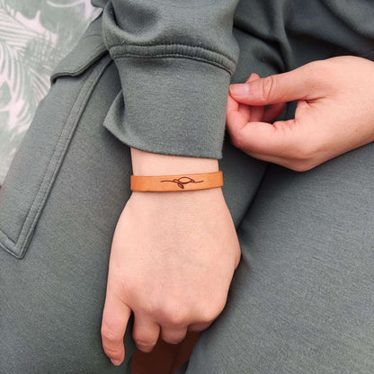 A brown leather bracelet with a sea turtle engraved on it.