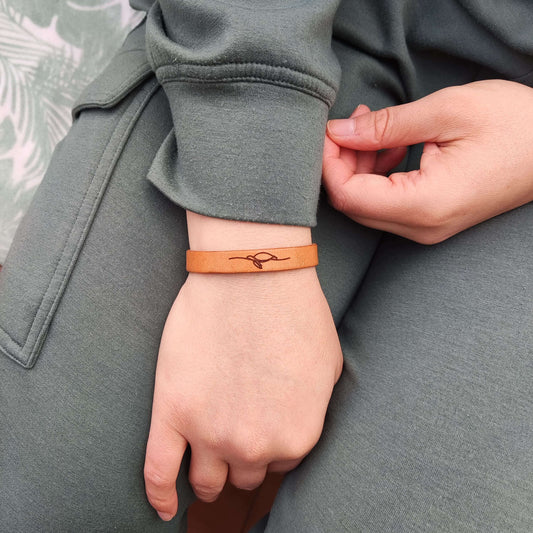 A brown leather bracelet with a sea turtle engraved on it.