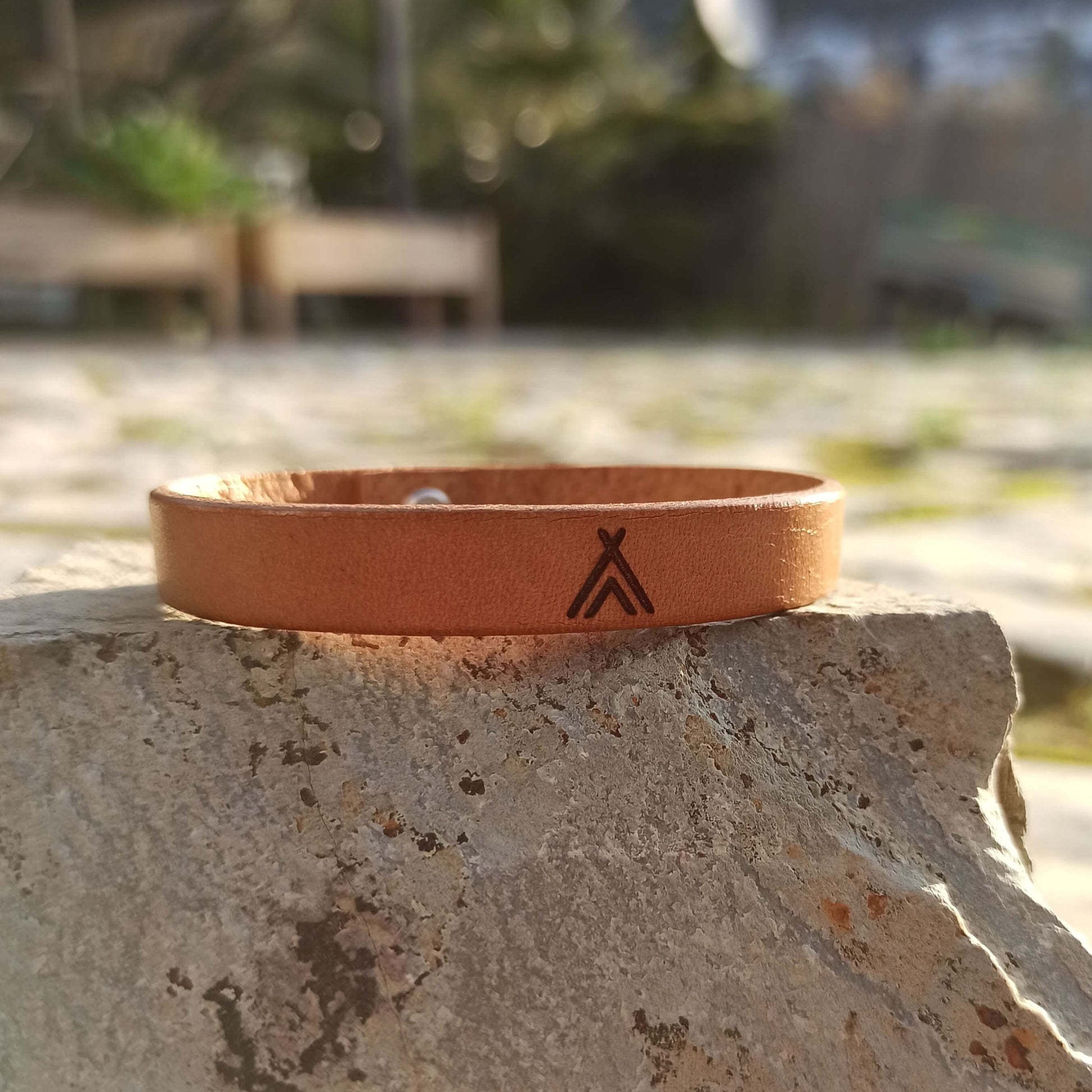 A brown leather bracelet with a tipi symbol engraved on it