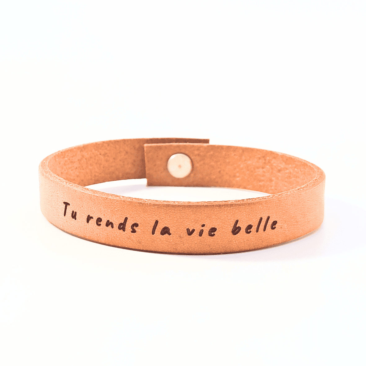 A brown leather bracelet with the text 'Tu rends la vie belle' engraved on it.