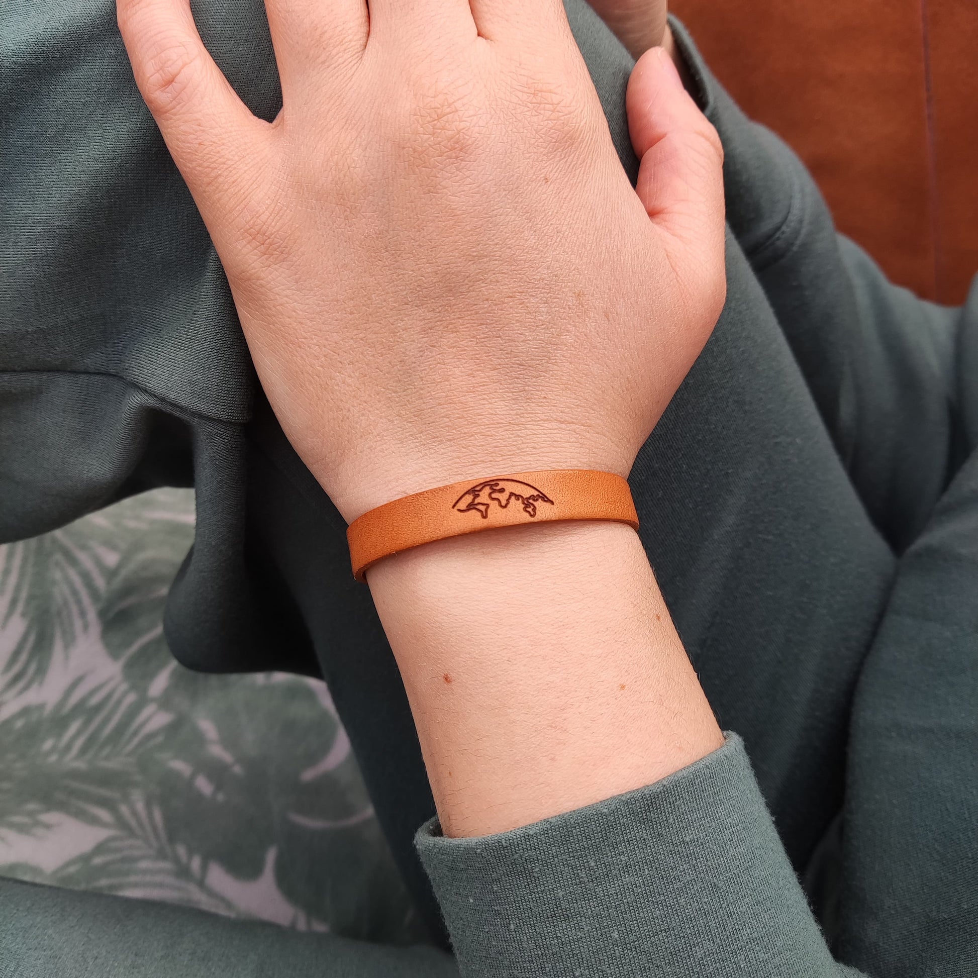 A brown leather bracelet with the world engraved on it.