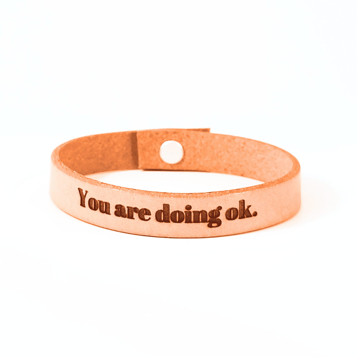A brown leather bracelet with the text 'You are doing ok.' engraved on it.