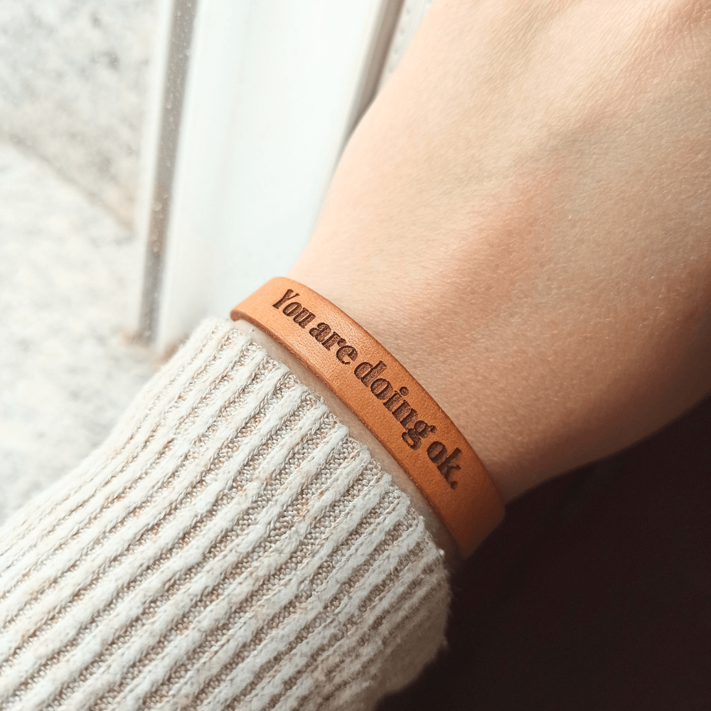 A brown leather bracelet with `You are doing ok´ engraved on it.