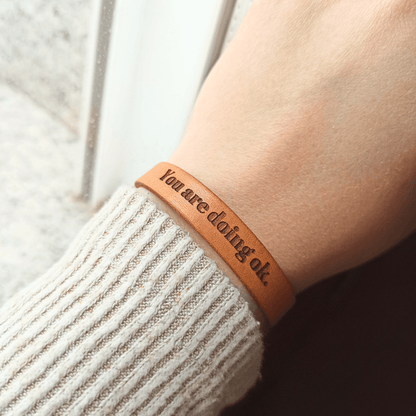 A brown leather bracelet with `You are doing ok´ engraved on it.