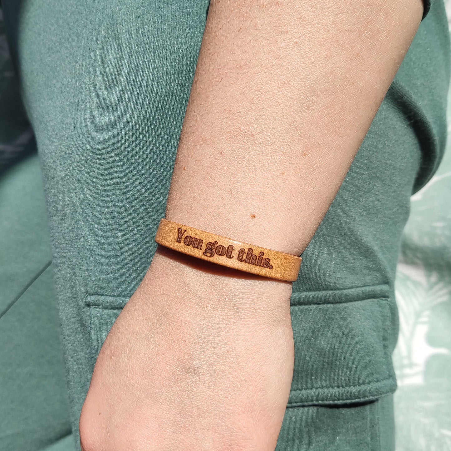 A brown leather bracelet with the text 'You got this.' engraved on it.