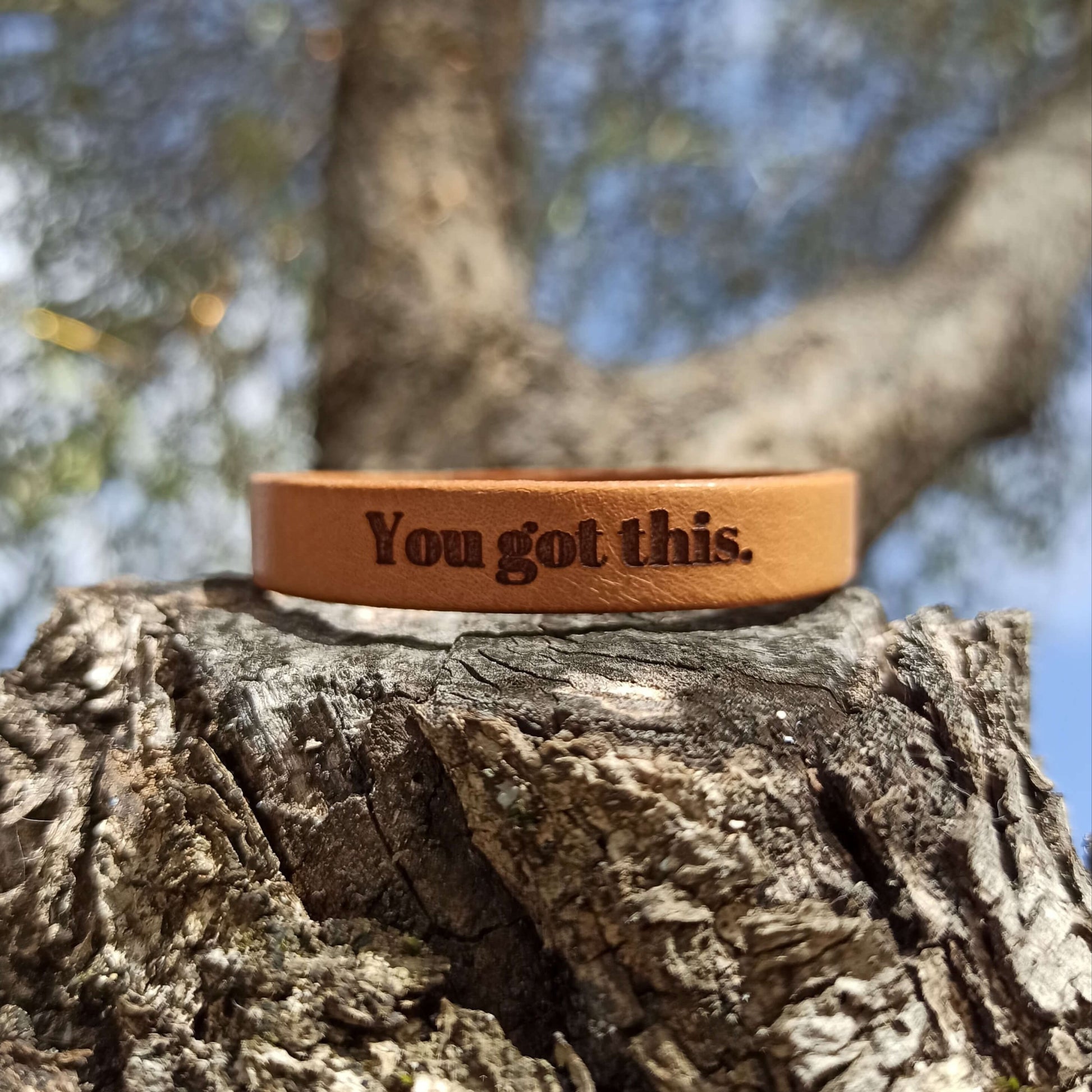 A brown leather bracelet with the text 'You got this.' engraved on it.